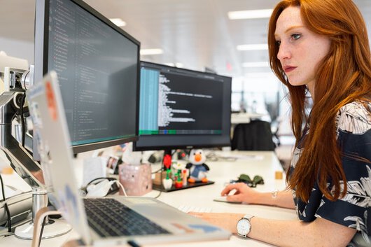 Mujer de perfil tecleando en un ordenador con dos pantallas.