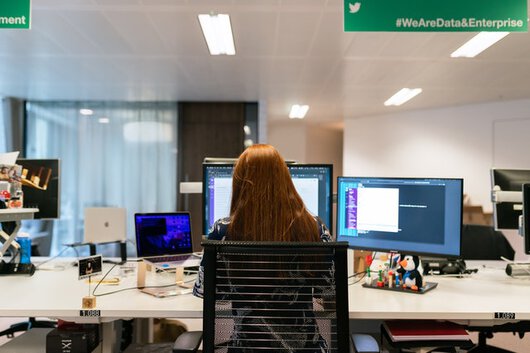Mujer sentada delante de un escritorio manejando ordenadores.